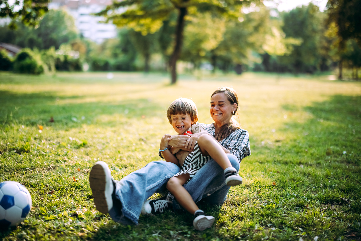 Photo of a female and young child playing with a ball outside on green grass