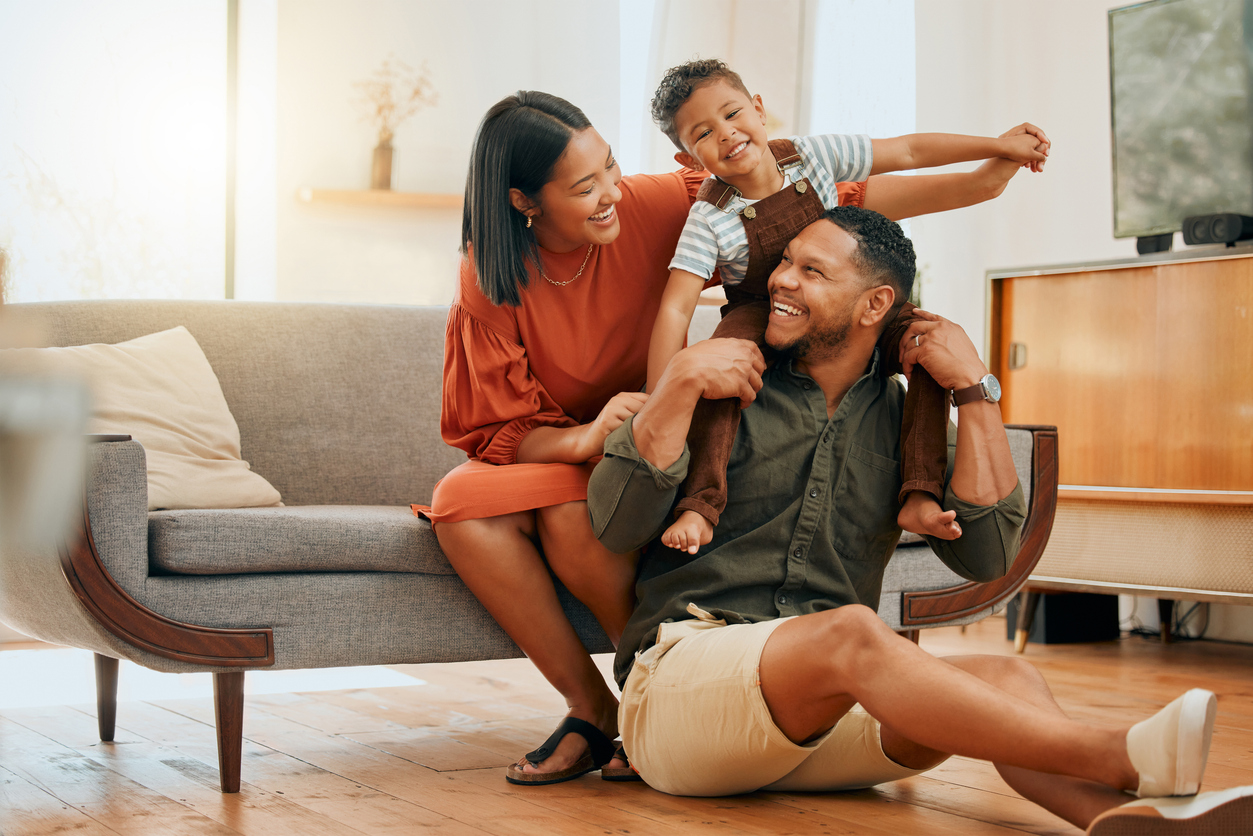 Photo of a female, young child and male playing together inside near sofa