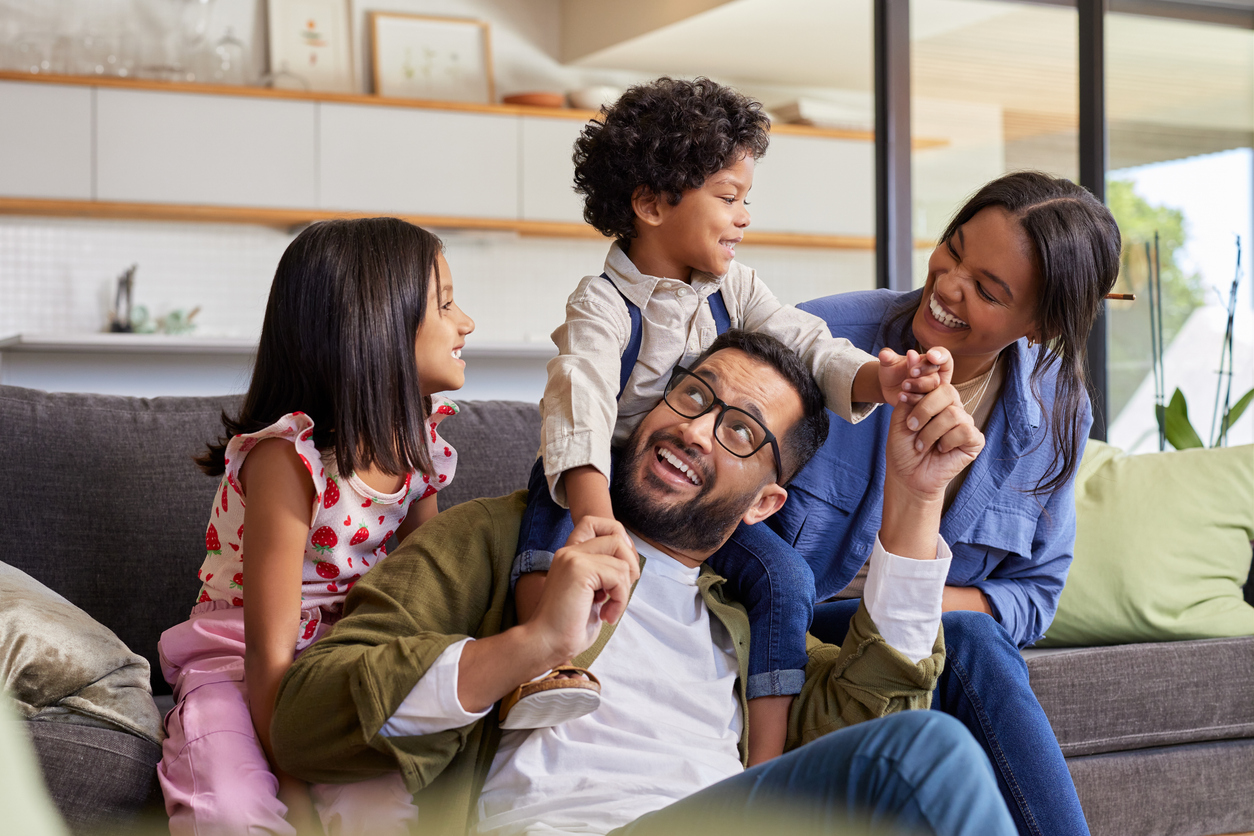 Photo of a female, young children and male playing together inside on a sofa